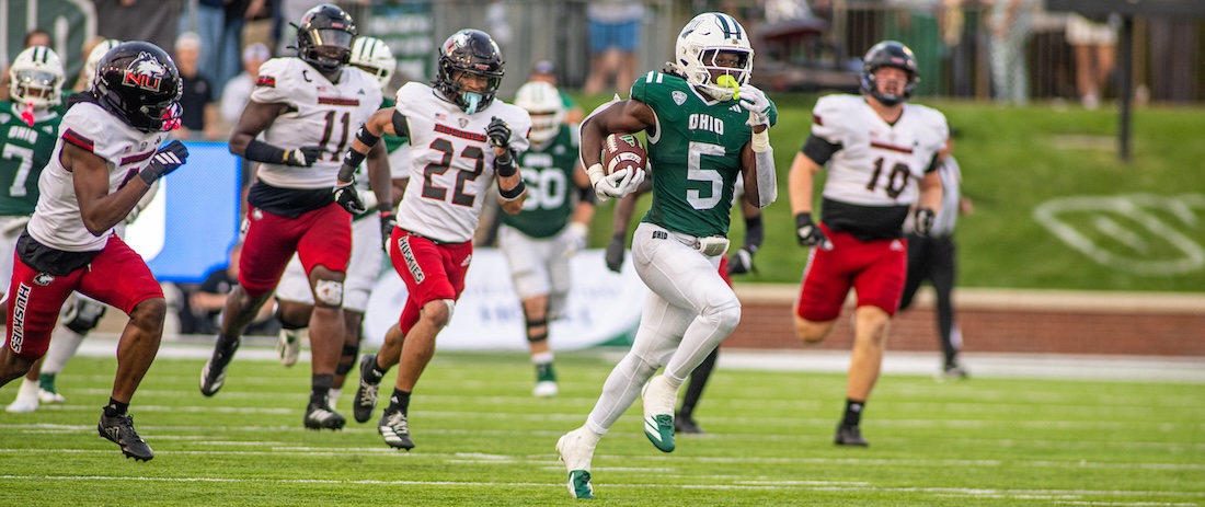 a Bobcat football player breaks away from defenders, carrying the ball