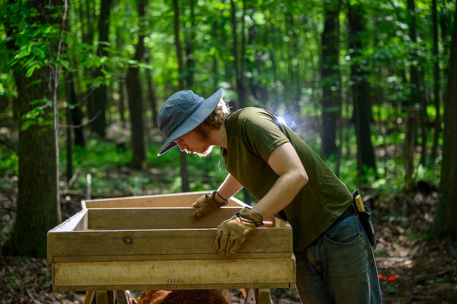A researcher leans over a device sifting through their findings at an archeological dig
