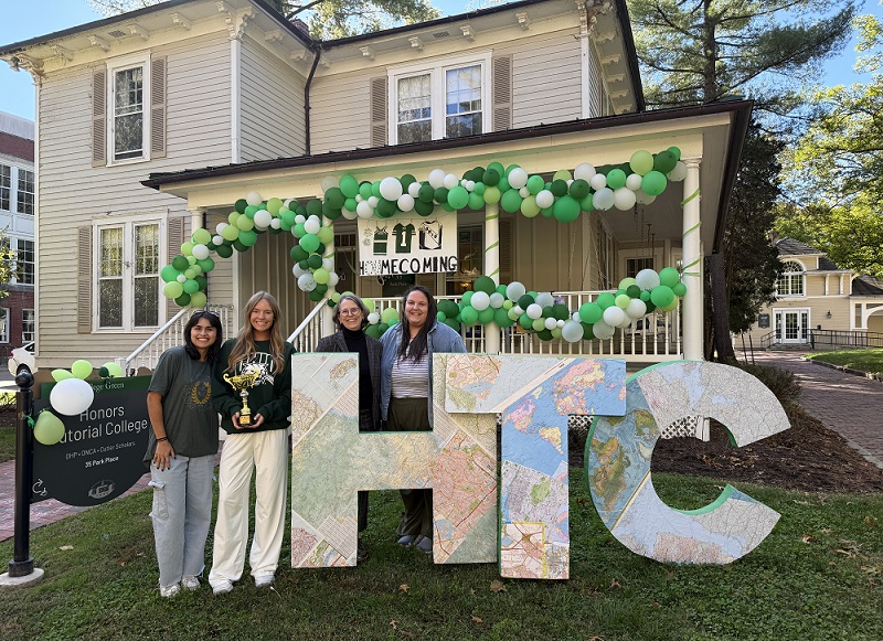 Honors Tutorial College representatives hold their trophy and stand together beside the giant HTC letters and in front of the HTC building