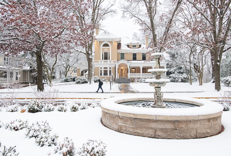 A student walks past Park Place in the snow, with a fountain the foreground