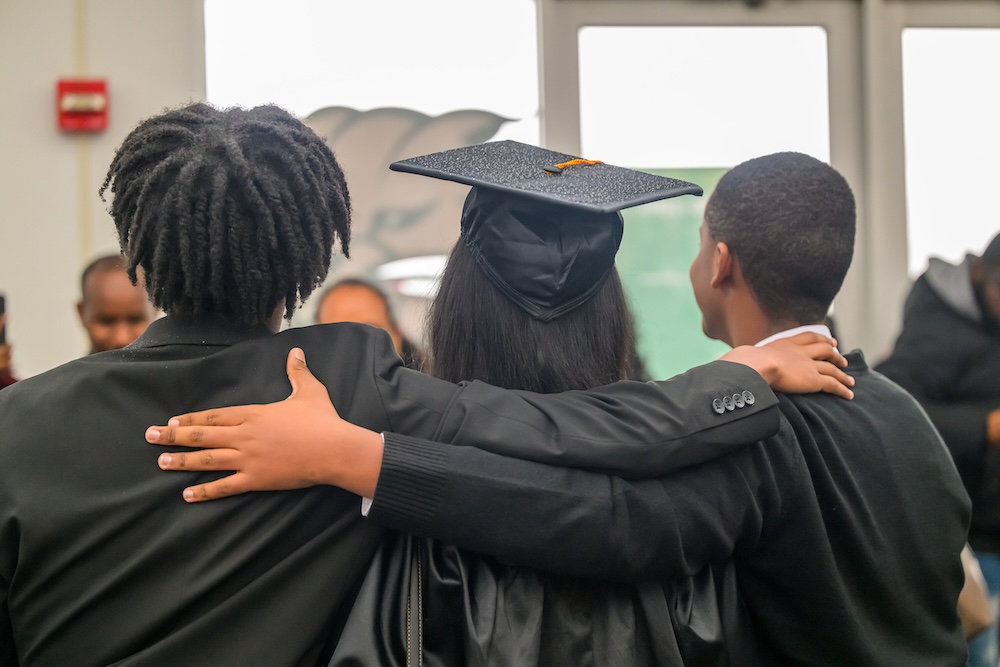 Three people, pictured from behind with their arms around each other, pose for a photo