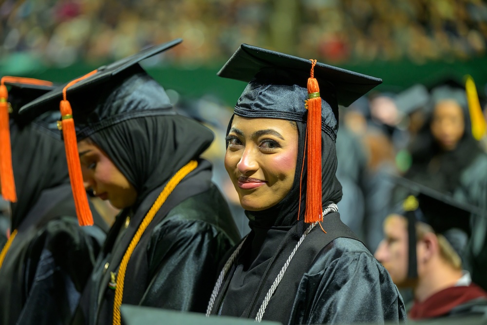 At the Commencement ceremony, a new graduate smiles at the camera
