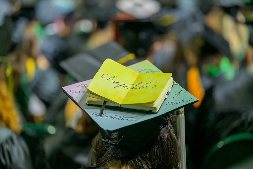 At the Commencement ceremony, a graduation cap with a small book attached reads "To the next chapter of our adventure"