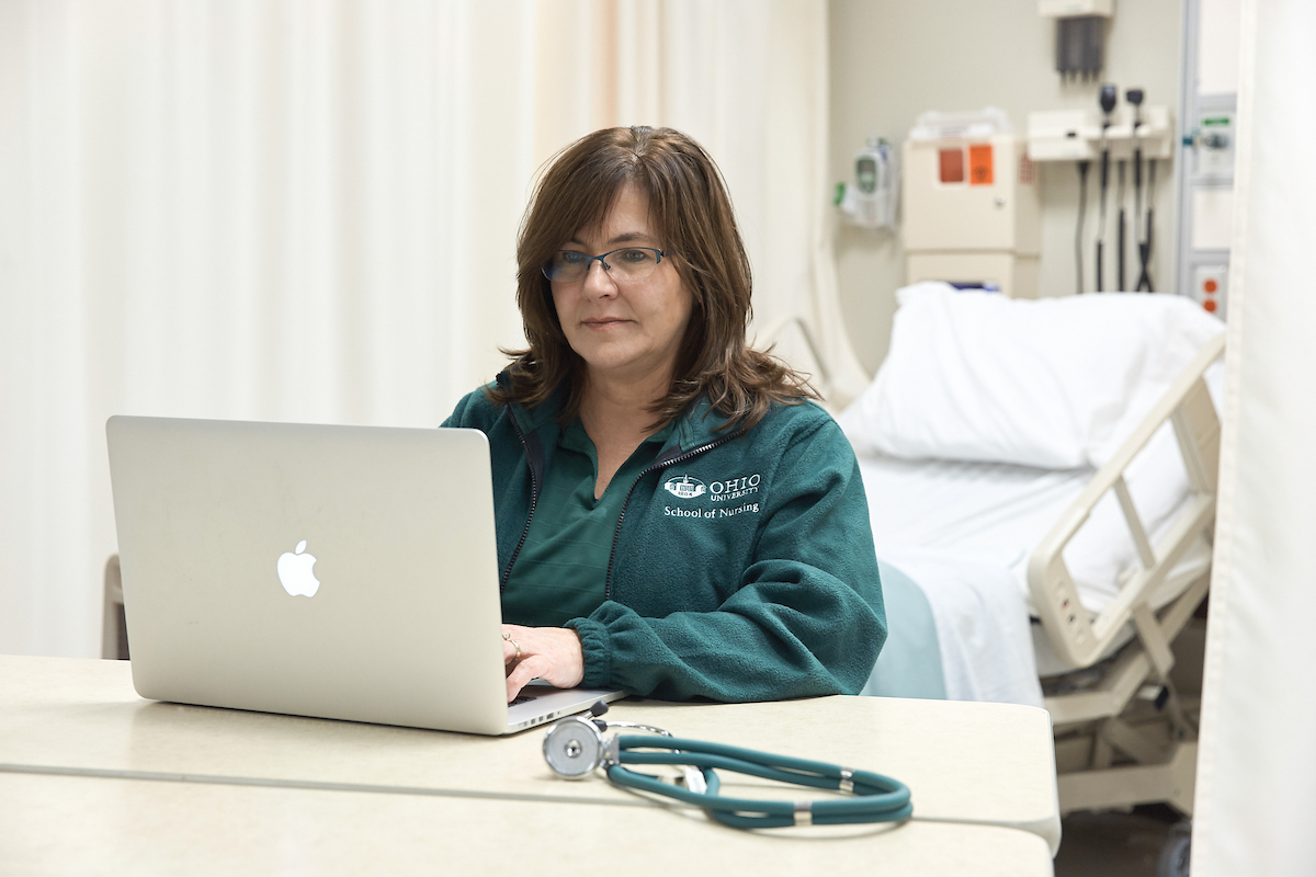 A nurse looks at a laptop in a hospital room