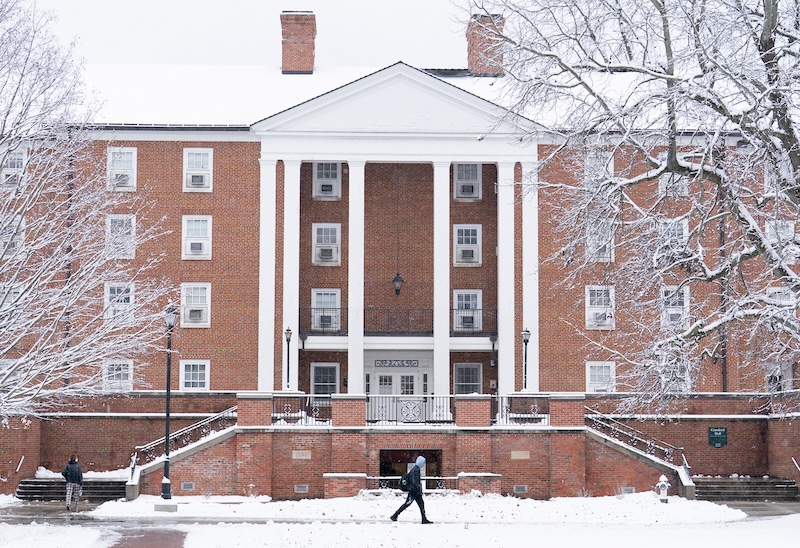 A studeny walks past a residence hall in the snow