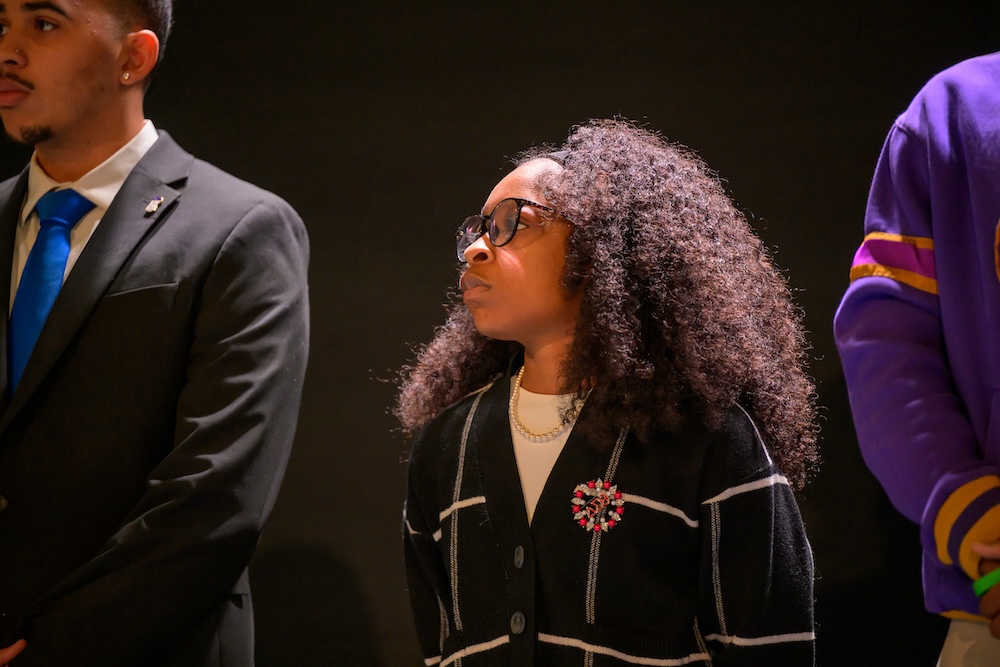 A student stands in a line, looking off to her right