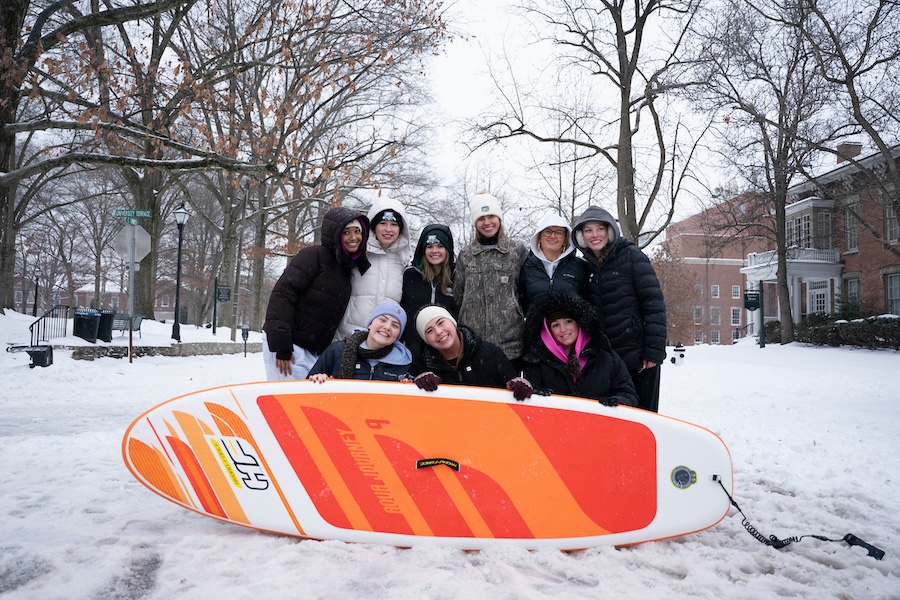 A group of people stand in a snowy street with an orange boogie board