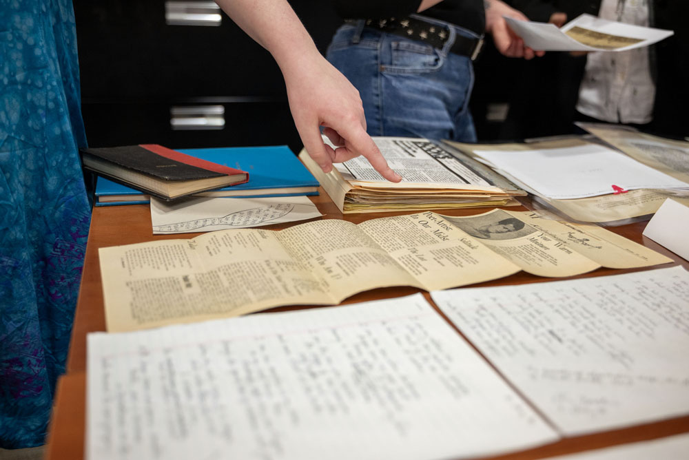 Someone pointing at yellowed, historical documents on a wood tabel.