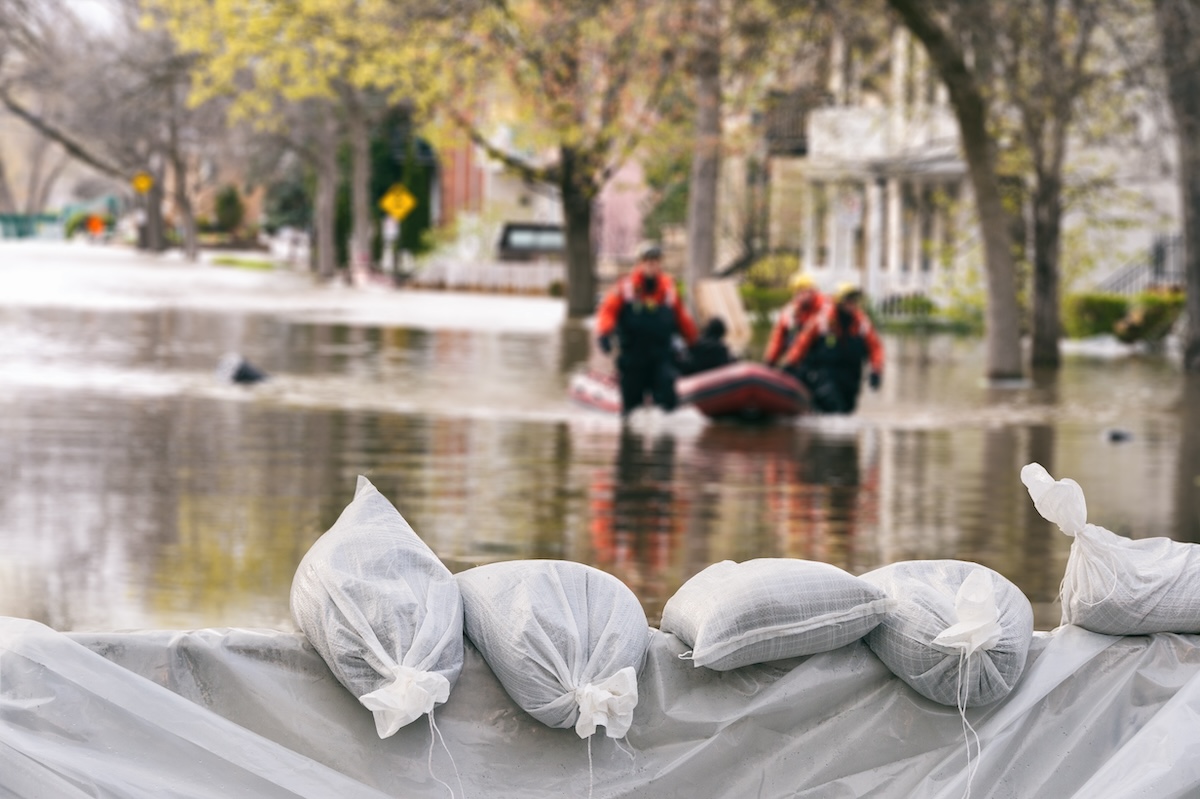 emergency workers wade through flood waters with sandbags in the foreground