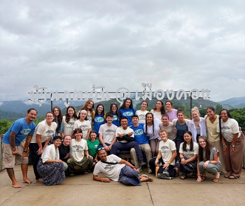 A group of people standing outside in front of a sign written in Thai.