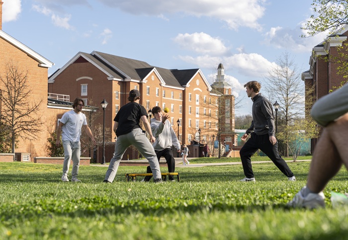 Four students play a game together and throw a ball into the air in the grass on a spring day at Ohio University