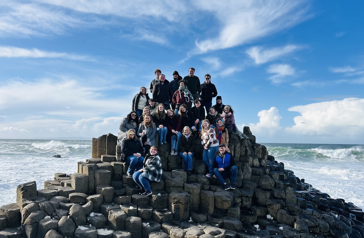 a large group of students poses for a picture by the seaside