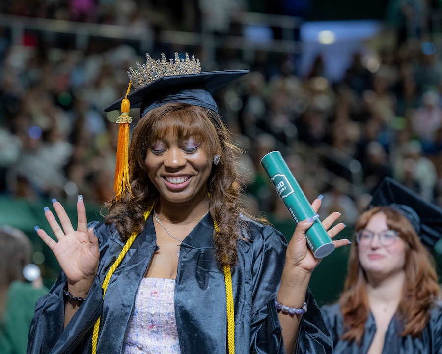 a student wearing a cap and gown poses happily holding her new diploma