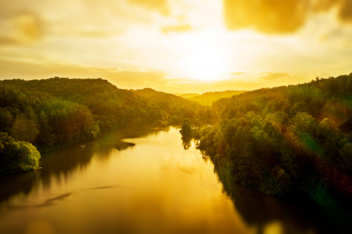 The sun is shown over Strouds Run State Park,  showing water and trees
