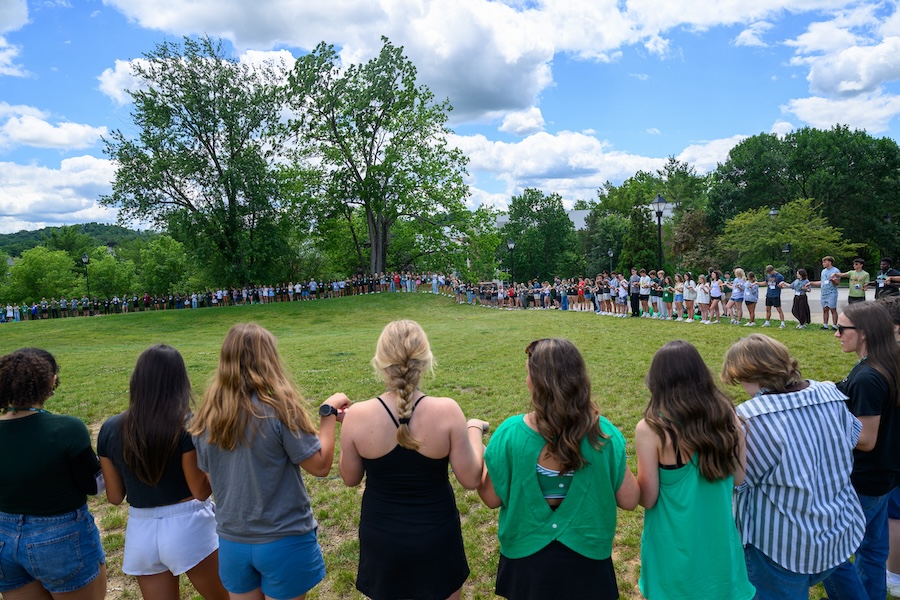 a very large group of students stand in a circle, holding hands