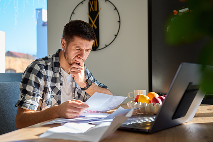 A man hunched over a laptop struggles with bills.
