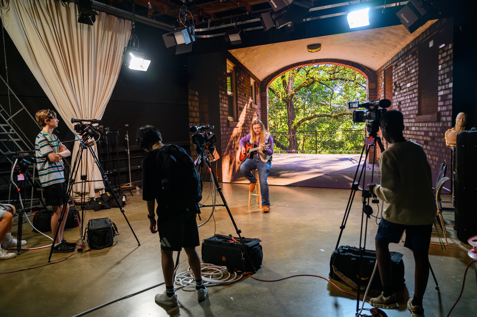 High School Media workshop participants take video and watch other production equipment while a musician plays a guitar on a set for a video