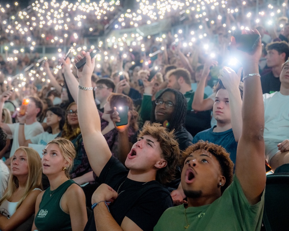 Students cheer in the Convo, holding up their cell phone flashlights