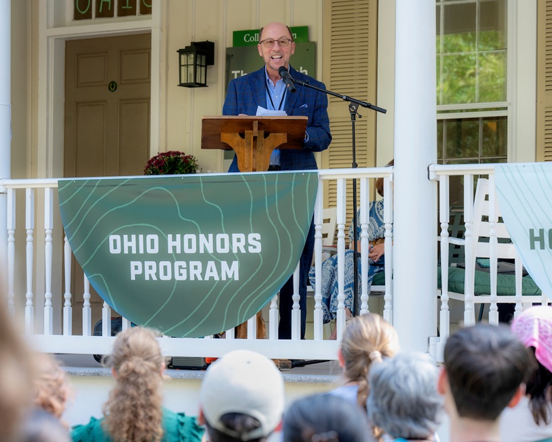 Bruce Burtch speaks to the crowd while standing on the porch at the dedication of the Burtch House
