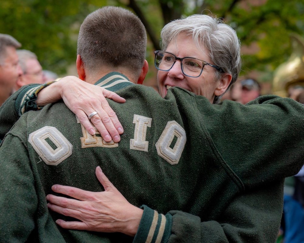 Marching 110 alumni band members embrace during the Homecoming parade