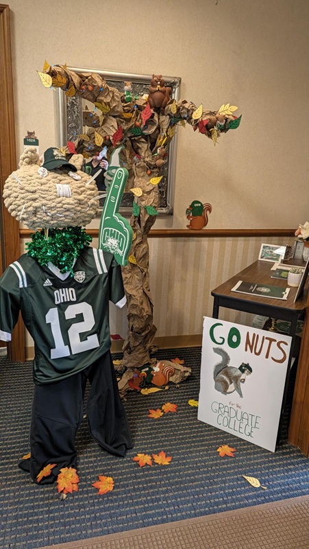 A decoration is made to look like an animal that is wearing an OHIO Football jersey near a sign  that says Go Nuts for the Graduate College, and a tree decoration is in the background
