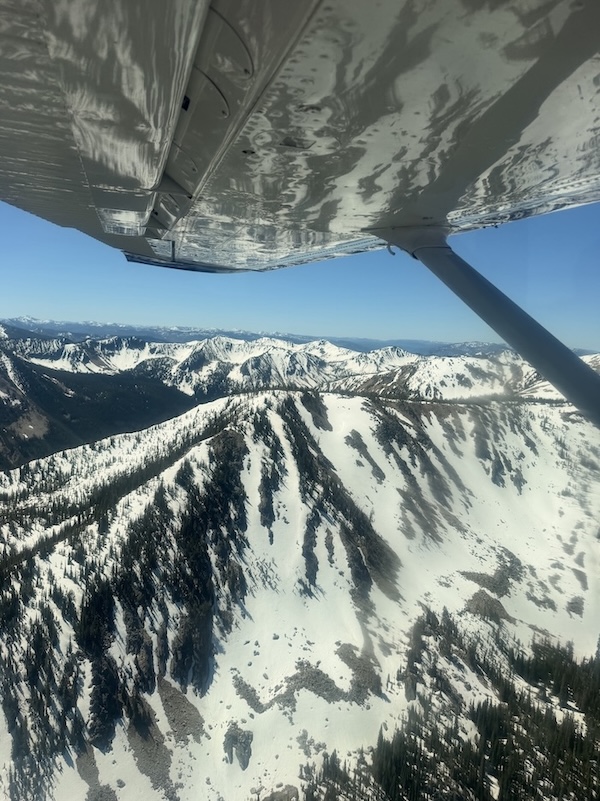 view of snow-capped mountains from an airplane with the wing in the foreground
