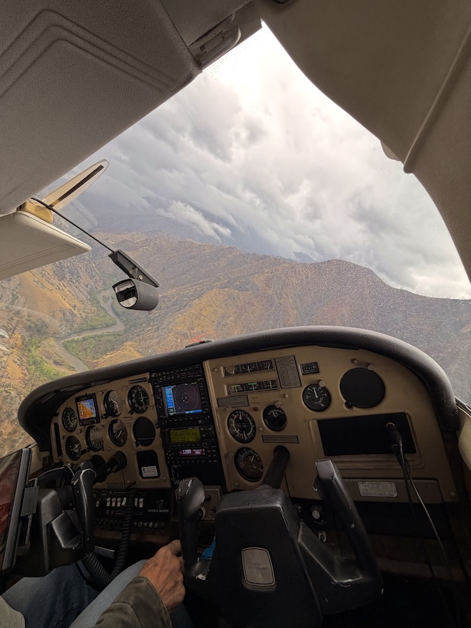 Mountains seen through the window of an airplane with the airplane controls and pilot's hands in the foreground