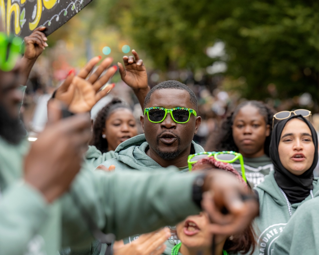 A man in green-framed sunglasses marches in the Homecoming parade