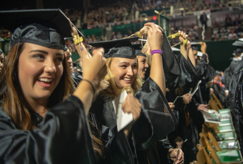 Kristine N. Pollard (left) and Carly Joy Pavey (center) move their tassels from right to left at Fall Commencement.