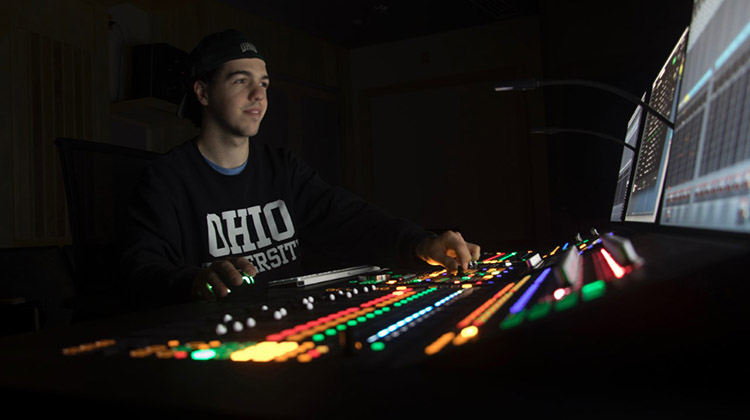 Christopher Pentecost, BSC ’19, is seen inside Ohio University’s Schoonover Center 448, the MDIA Sound Post-Production and Listening Lab, where he spent countless hours as an undergraduate mastering the skill of creating and editing the mosaic of sounds that bring stories to life.