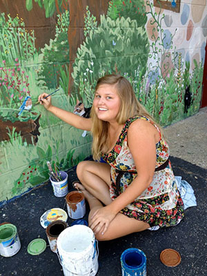 Laura (Brooks) Valls, BFA ’12, is pictured in the summer of 2012, painting a mural at The Farmacy in Athens.
