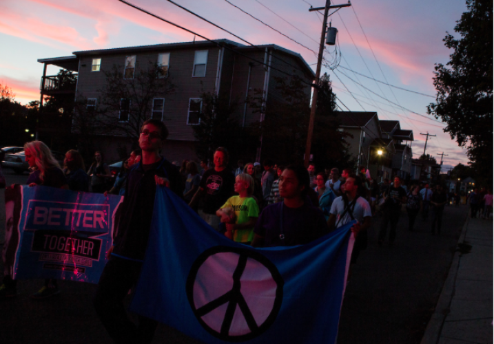 With their faces illuminated by police car lights, Ohio University students and Athens residents participate in the Interfaith Peace Walk through the city at sunset on Sept. 11, 2014