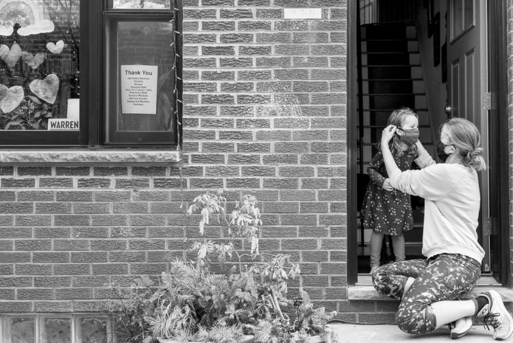 A woman puts a face mask on a young girl's in a front door way