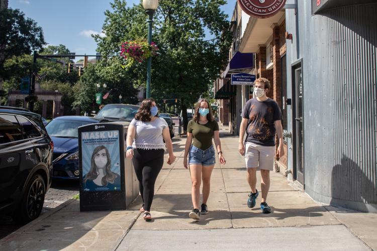 Three students wearing masks walking in down a sidewalk in Athens