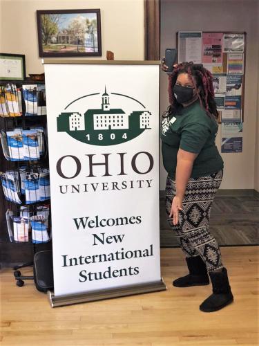 Shauna Torrington poses by sign that reads Ohio University Welcomes New International Students