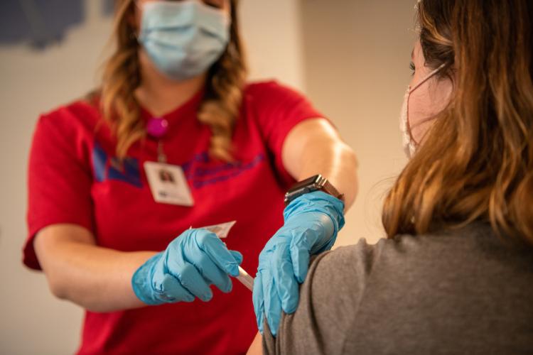 An Athens-City County Health Department worker gives a community member facing away from the camera a vaccine shot