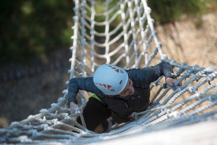 A woman climbs ropes to a zipline course on The Ridges