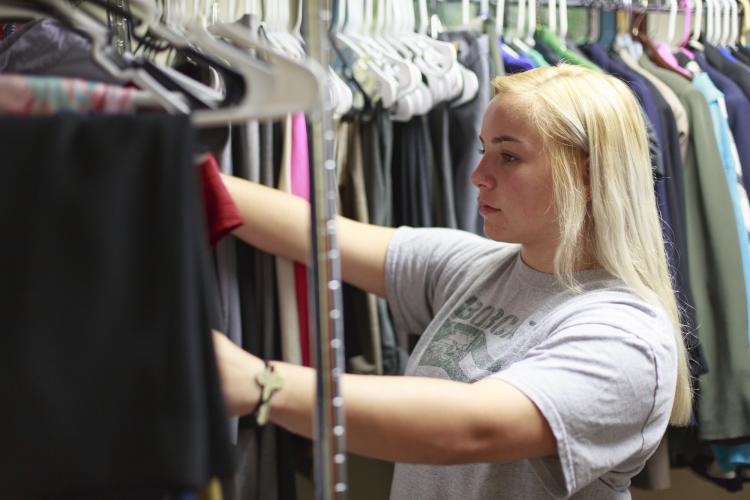 A student with long blonde hair looks through racks of clothing