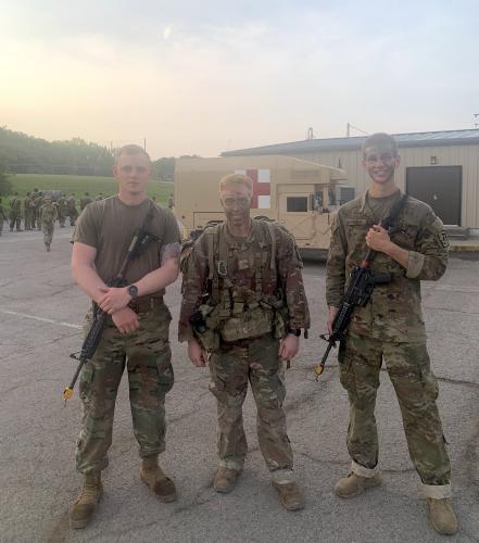 Three men stand in military camo, smiling for a picture