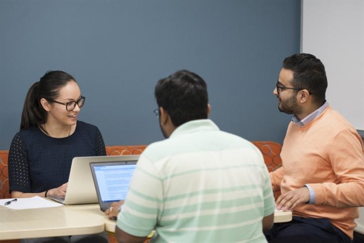 Three students working on laptops around a table