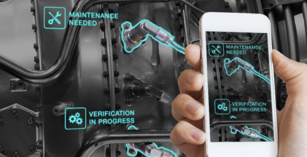 A mechanical part in the background with a phone screen in front displaying that maintenance is needed on a specific part as well as verification another part is good