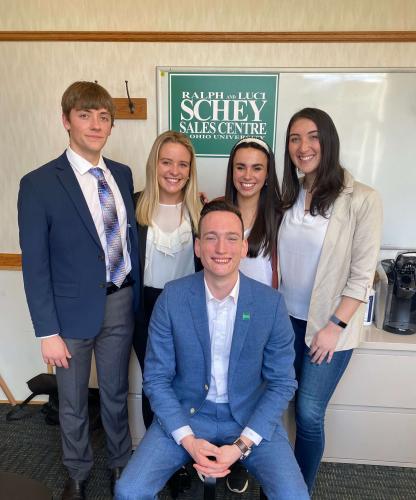 Four students stand behind a mentor who is sitting down