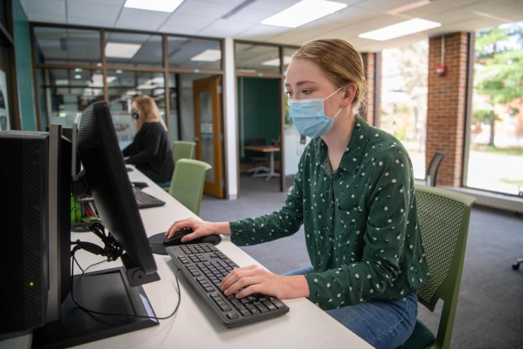 A student working on a computer and wearing a mask