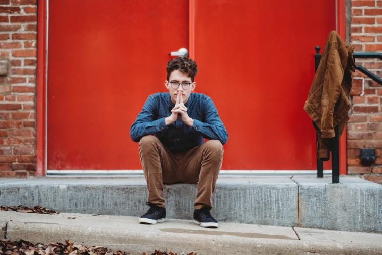 Sam Brandes sits on a step with a red door behind him.