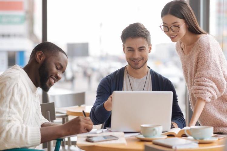 Three people meet at a table and work on a computer together