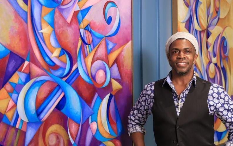 Cedric Michael Cox standing in front of one of his colorful, abstract paintings