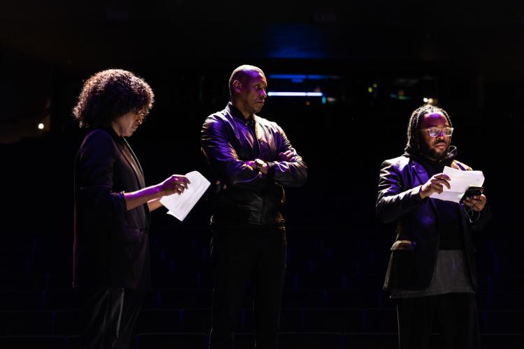 Three people stand in a dark room with light illuminating their faces.