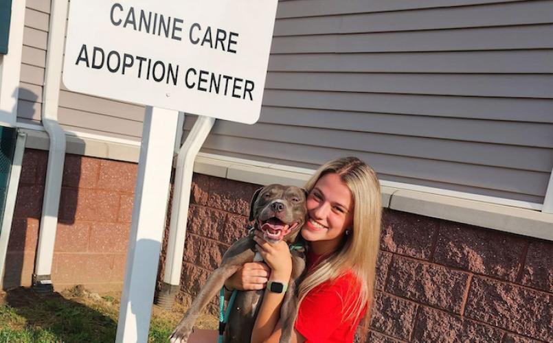 Jess Mitchell holding a dog in front of a sign that says 