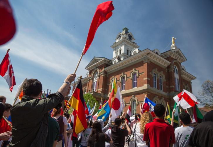 People wave flags from various countries during the International Street Fair in Athens, Ohio. The Japanese flag is featured in the center.
