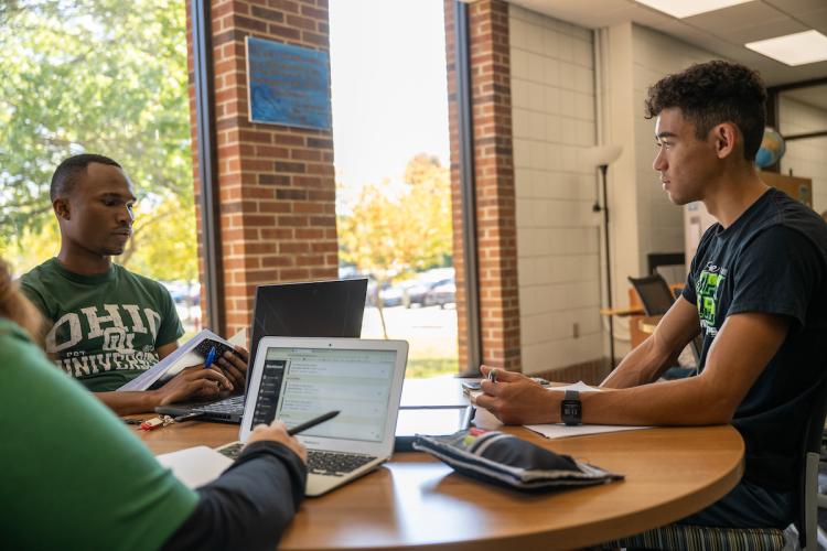 Three students sit at a table with laptops in the student success center